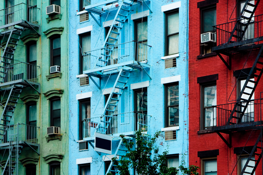 Three colorful, red, blue and green, apartment buildings facades with emergency escapes. Typical New York City, Boston or Chicago rental complexes with fire escape stairs next to the windows.